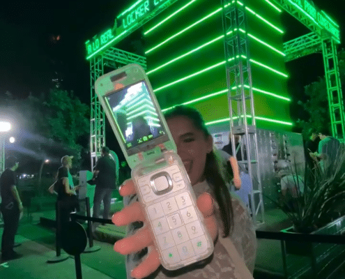 Stand de Heineken de fondo con una asistent a evento mostrando el celular de The Boring Phone